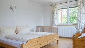 Een slaapkamer met een houten bed, een radiator, een raam met gordijnen en een hartvormige decoratie aan de muur.