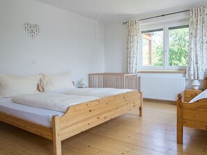 Een slaapkamer met een houten bed, een radiator, een raam met gordijnen en een hartvormige decoratie aan de muur.
