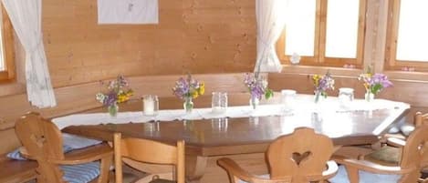A wooden cabin interior with a round dining table, six wooden chairs, and floral centerpieces.