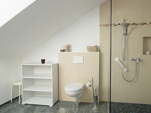 A bathroom with a shower, toilet, and a white shelf unit.