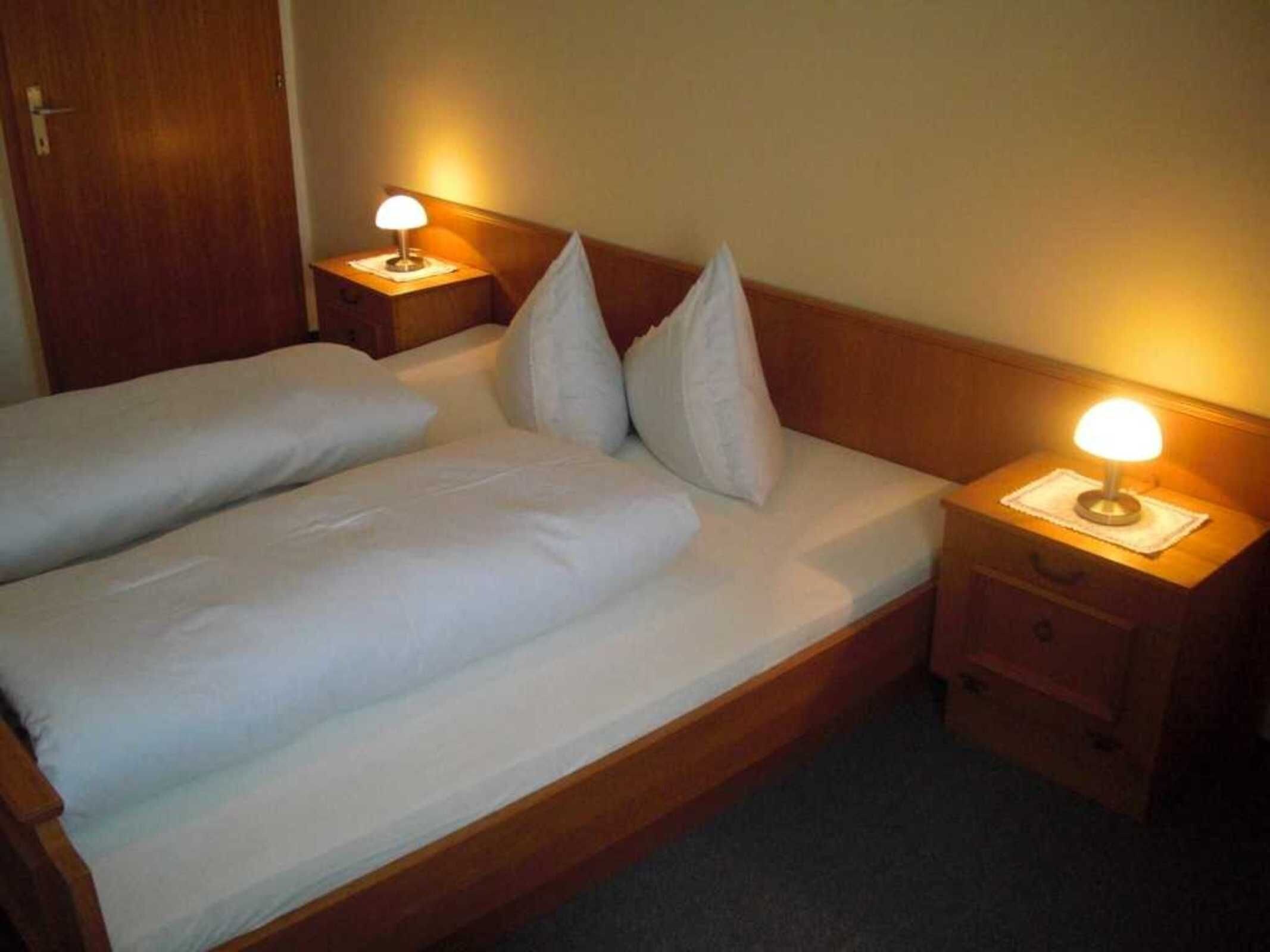 Ein Doppelbett mit weißer Bettwäsche, zwei Nachttische mit Lampen und ein Holzkopfstück.
