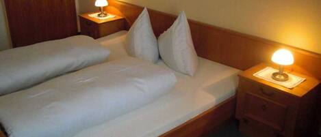 A double bed with white bedding, two bedside tables with lamps, and a wooden headboard.