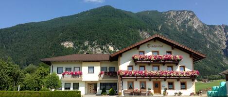 A two-story building with a sign reading 'Tischertschot' in front of a mountainous backdrop.