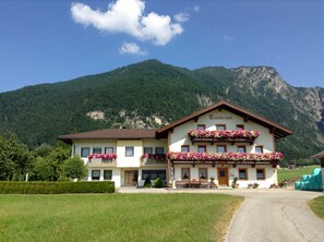 Ein zweistöckiges Gebäude mit einem Schild, auf dem 'Tischertschot' steht, vor einer gebirgigen Landschaft.