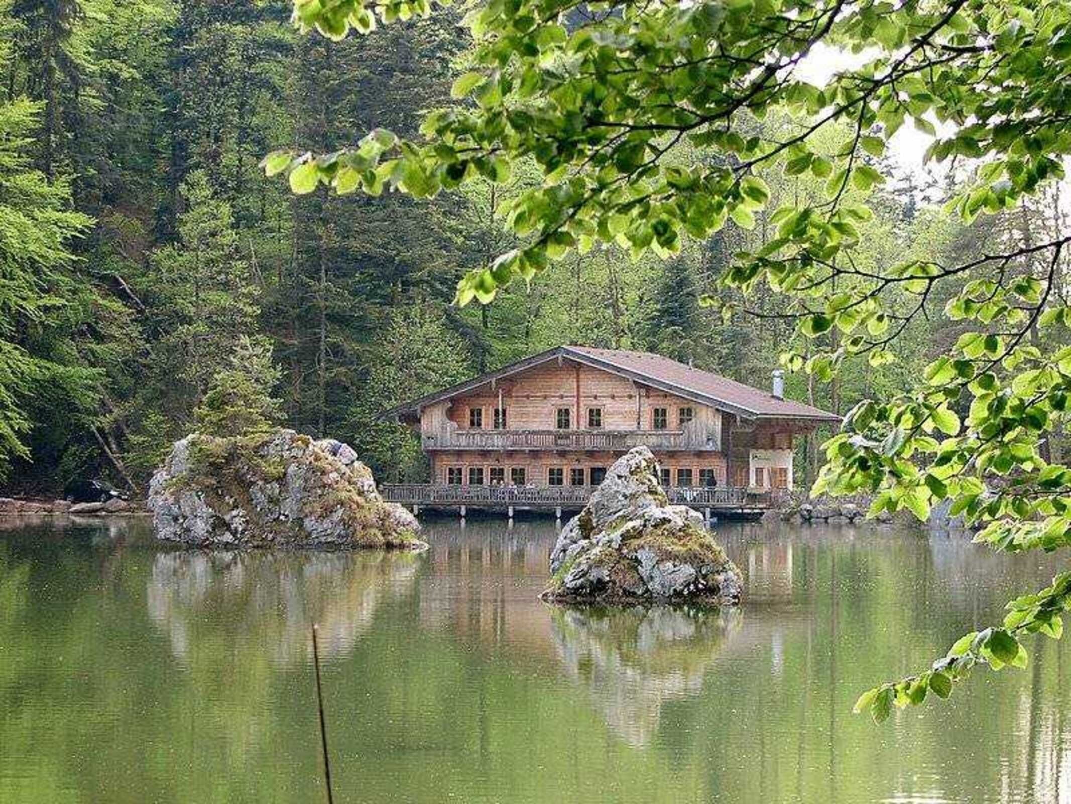 Un chalet en bois doté d’un balcon, situé au bord d’un lac paisible, avec deux rochers imposants en premier plan.