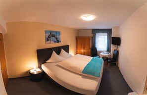 A hotel room with a bed, bedside lamp, a small table with a chair, a TV mounted on the wall, and a window with curtains. - Double room 3 - TISCHLERHOF in Breitenbach am Inn (Breitenbach am Inn)