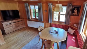 Ein gemütliches Cabin-Interieur mit einem Holzesstisch, einem Fernseher auf einem Schrank und einer roten gepolsterten Bank an den Fenstern.