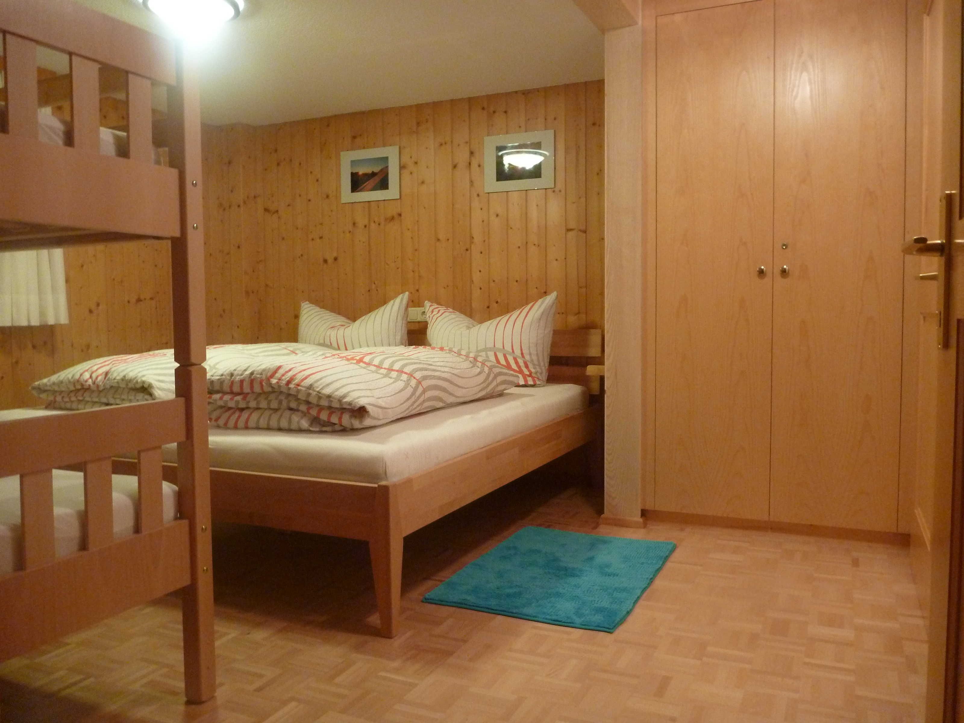 Une pièce avec un lit superposé, un lit simple, des murs en bois, une porte et un petit tapis.