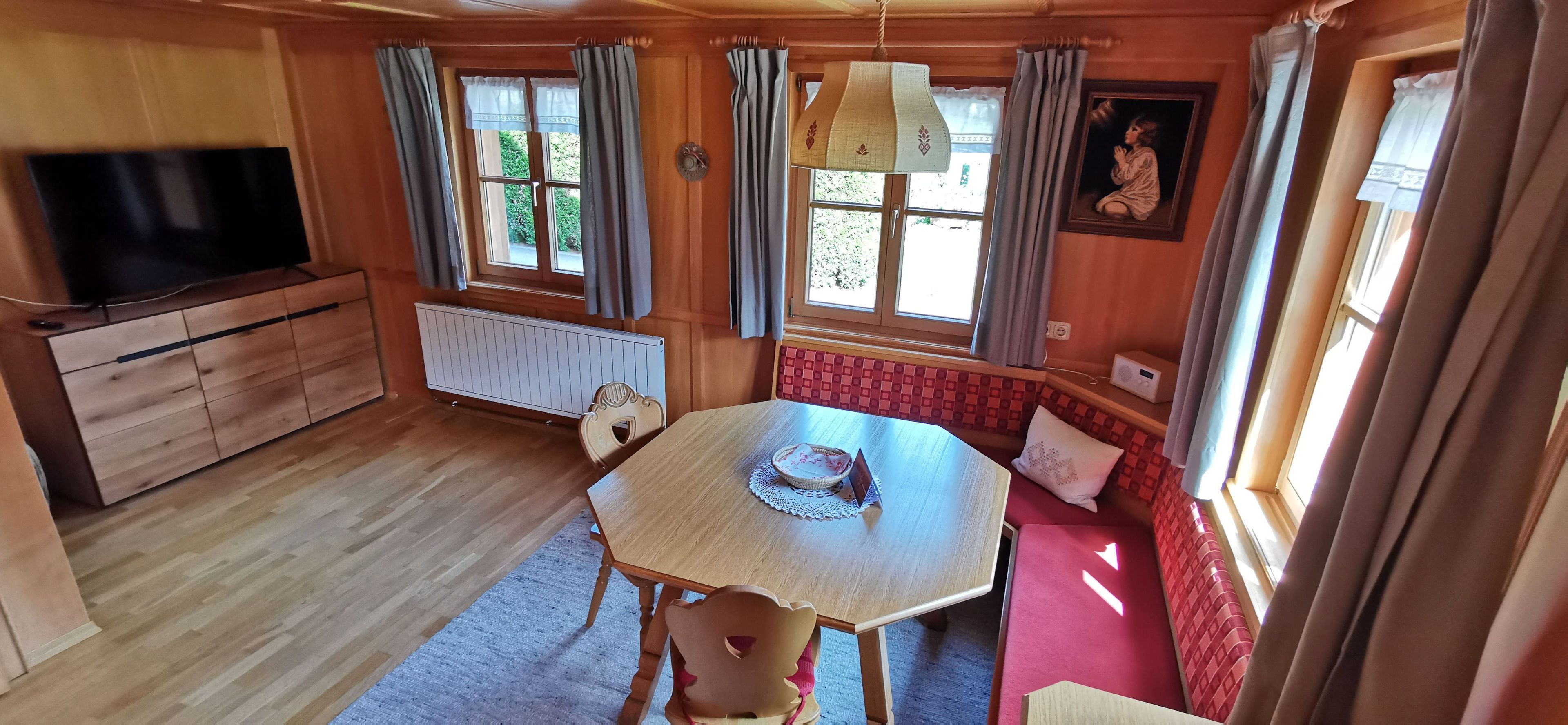Een gezellig cabin interieur met een houten eettafel, een televisie op een kast, en een rode, beklede bank bij de ramen.