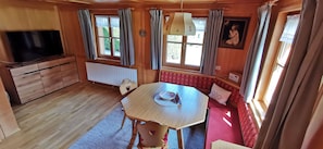 A cozy cabin interior with a wooden dining table, a television on a cabinet, and a red cushioned bench by the windows. - Vacation with Moses - Holiday apartment (Schoppernau)