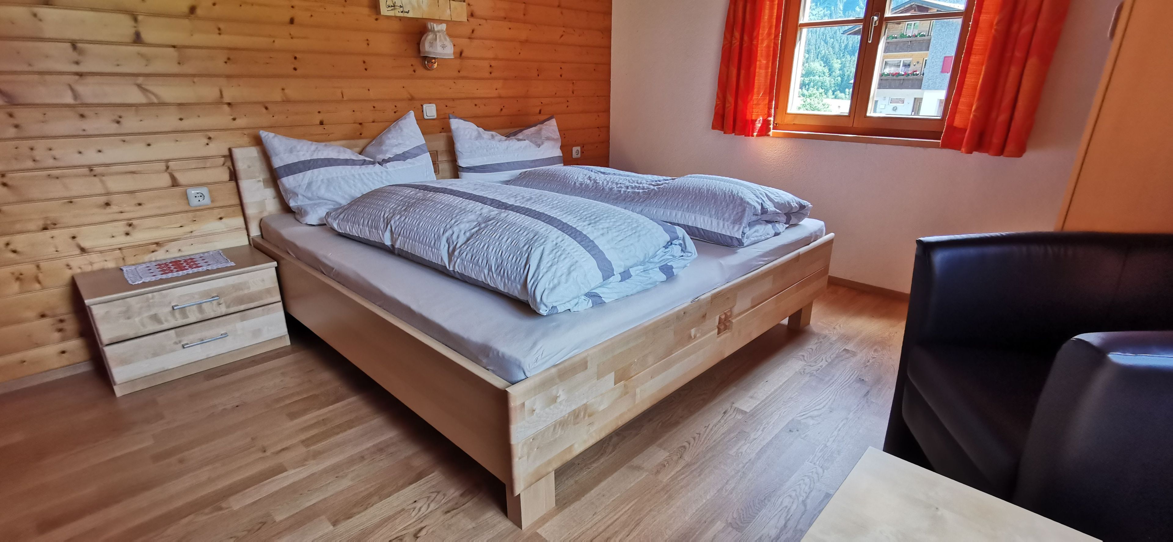 Un lit en bois avec une tête de lit, deux tables de chevet et une fenêtre avec des rideaux.