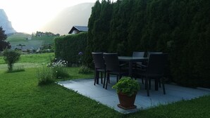 Eine Terrasse mit Gartenmöbeln, einem Blumentopf und einer Hecke.
