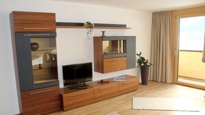 A modern living room with a flat-screen TV, wooden cabinets, and a sliding glass door to the right. - Hochalpe APP#3 - Ritter Anni - Haus Ritter (Schoppernau)