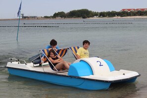 Ein kleines Motorboot mit zwei Personen und einem Kind, in Blau und Weiß gehalten, mit der Aufschrift '2' vorne und einer Fahnenstange mit einer Flagge.
