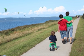 Une promenade en bord de mer avec un sentier bordé de gazon, un enfant sur un tricycle et des gens qui se promènent.