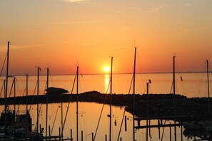 Un port de plaisance où sont amarrés de nombreux bateaux, un ciel dégagé et le soleil qui se couche à l’horizon.