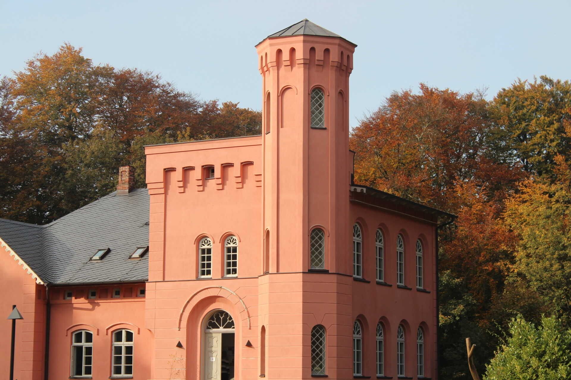 A pink building with a tower, arched windows, and a door.