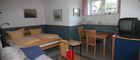 Ein Zimmer mit einem Bett, einem kleinen Schreibtisch mit Fernseher, einem Sessel und einem Sofa.