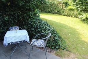 Ein Sitzbereich im Freien mit Tisch und zwei Stühlen, umgeben von viel Grün.