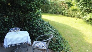 An outdoor seating area with a table and two chairs, surrounded by greenery. - Whg. 4 Swamp swallow basement - Haus Feldmann (Lohme)