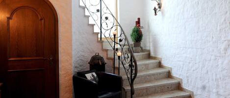 Una escalera con barandilla de hierro forjado, una puerta de madera, un sillón de cuero negro y una pequeña planta en maceta.