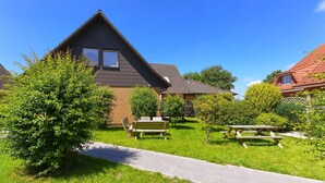 Une maison d’habitation avec un toit en pente, une cour avant avec une table de pique-nique et des bancs, et un ciel bleu dégagé.