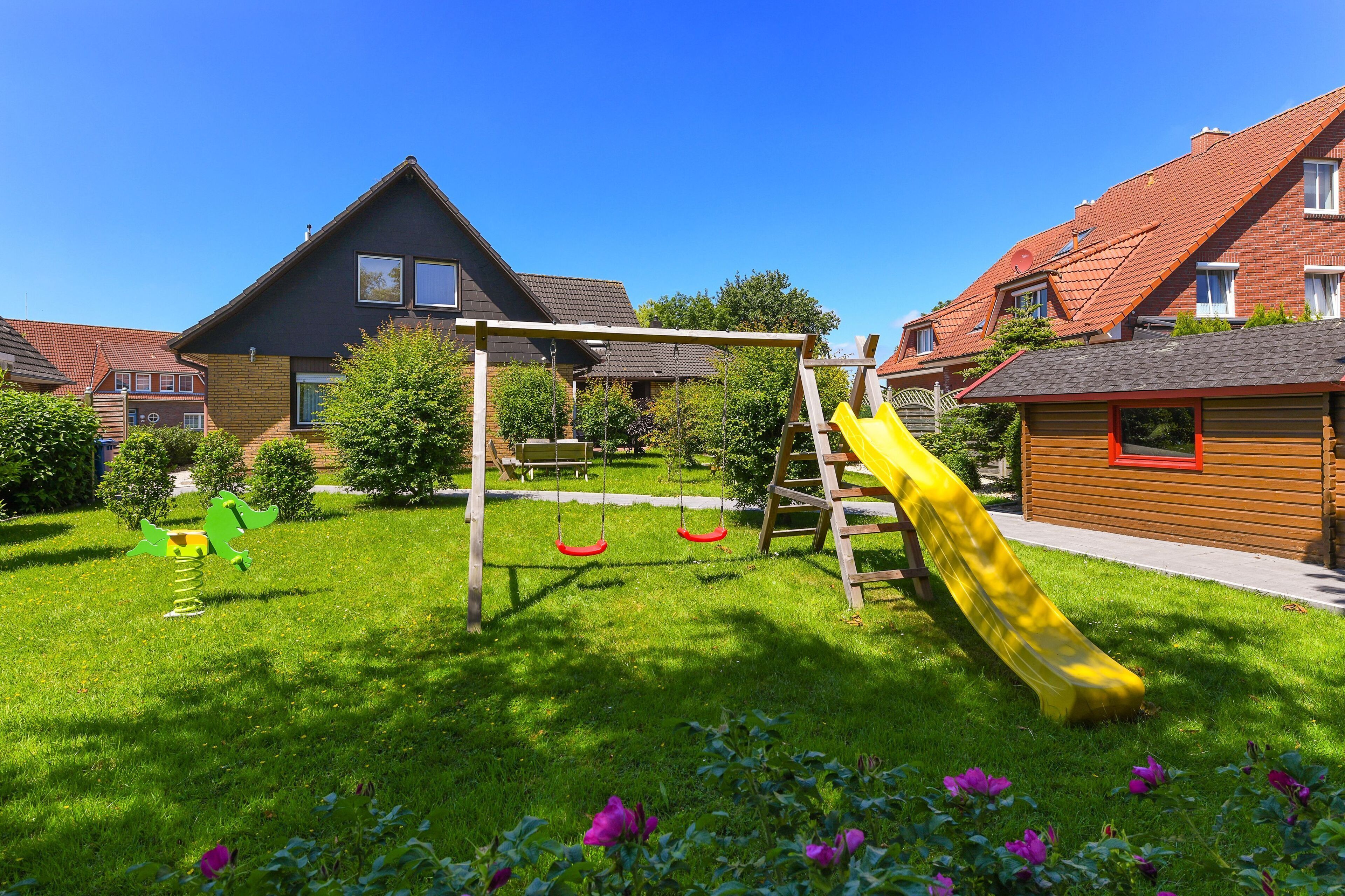 Zona residenziale con un parco giochi, comprensivo di altalene e scivolo, circondata da case con tetti in tegole rosse.