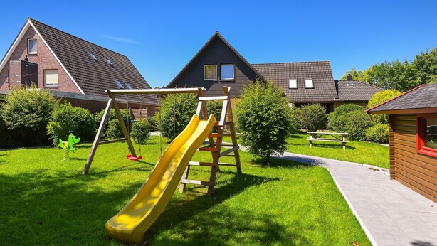 Un quartier résidentiel doté d’une aire de jeux comprenant un toboggan jaune, une balançoire en bois et une échelle.