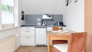 Une cuisine compacte avec des meubles blancs, un four à micro-ondes, une machine à café et une petite table à manger avec une chaise.