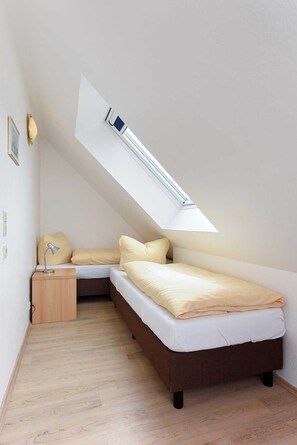 Une petite pièce avec un plafond en pente, comprenant un lit, une table de chevet et une lampe de bureau.