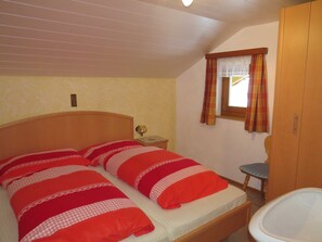 Un dormitorio con cama, mesita de noche, ventana con cortinas y un armario de madera.