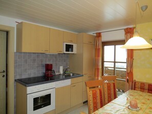 A kitchen with a microwave, oven, and coffee maker. There is a dining table with chairs and a lamp. - Apartment 1 - Biohof Haus Wieser (Abtenau)