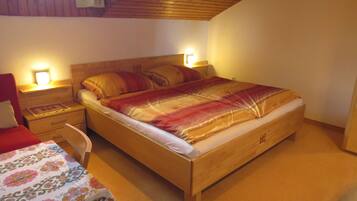 Ein Schlafzimmer mit einem Holzbett, zwei Nachttischen mit Lampen, einem Sessel und einer blumengemusterten Tagesdecke.