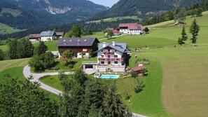 Una casa grande con piscina, rodeada de campos verdes exuberantes y montañas.