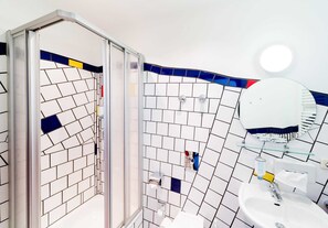 Een badkamer met een betegelde muur, een glazen douchecabine, een wastafel en een spiegel.