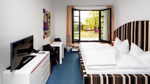 Hotelkamer met een bed, een bureau met een computer, een televisie en een raam met gordijnen.