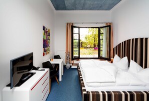 A hotel room with a bed, a desk with a computer, a TV, and a window with curtains. - Classic double room with terrace - artHOTEL Magdeburg GmbH (Magdeburg)