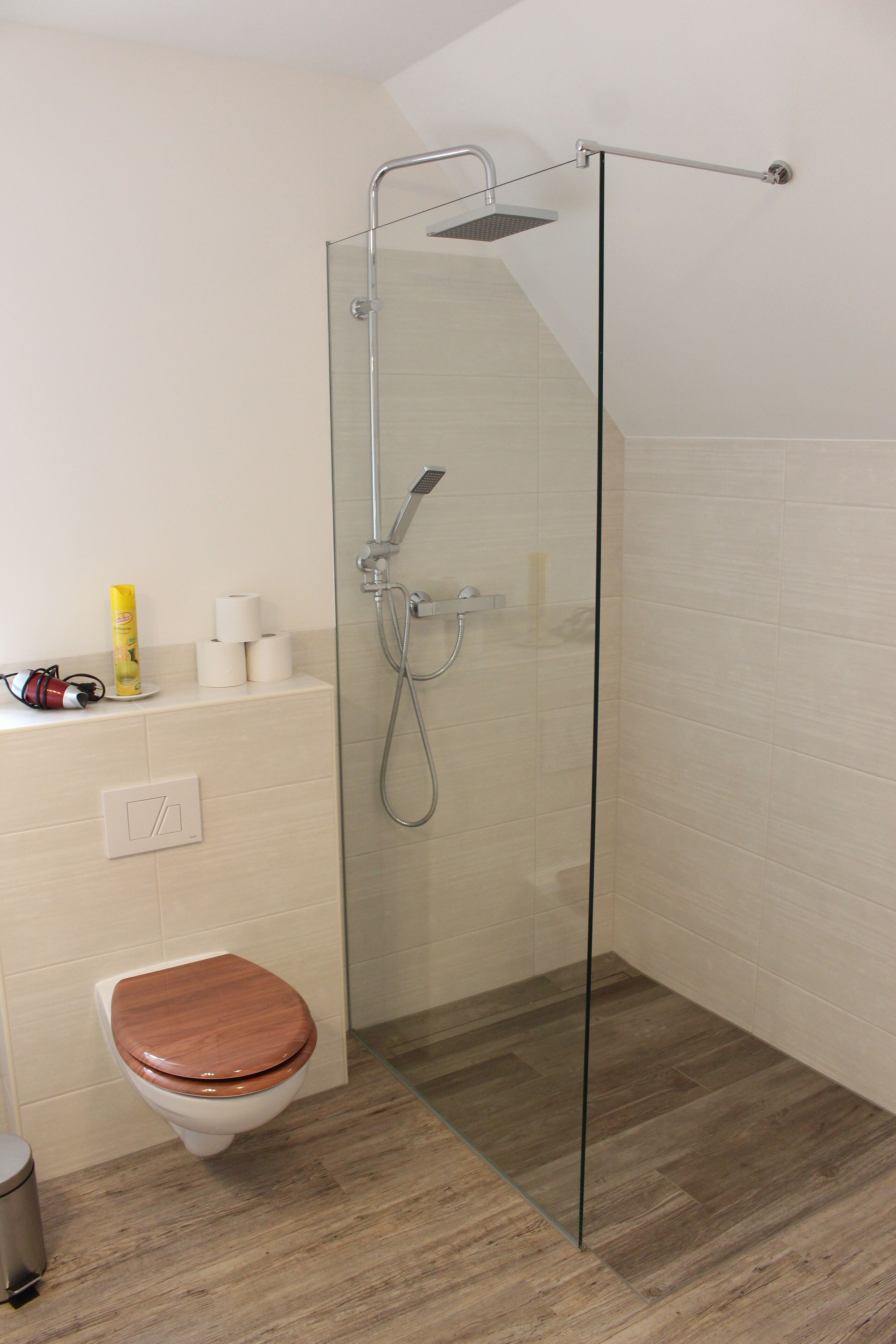 A modern bathroom with a glass-enclosed shower, a wooden toilet, and a white sink.