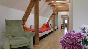 A room with a wooden ceiling, a bed with orange bedding, a green armchair, and a wooden floor. - Cozy accommodation in the Vierseithof in an idyllic, rural location (Crostwitz)