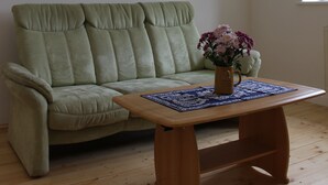 A room with a wooden ceiling, a light green sofa, a wooden coffee table with a vase of flowers, and a window. - Cozy accommodation in the Vierseithof in an idyllic, rural location (Crostwitz)