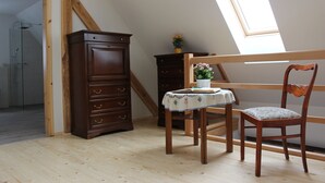 A room with a wooden floor, a wooden chair, a small table with a tablecloth, a wooden cabinet, and a skylight. - Cozy accommodation in the Vierseithof in an idyllic, rural location (Crostwitz)