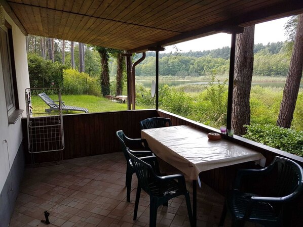A covered patio with a table and chairs, overlooking a lush landscape with trees and a body of water. - Vacation home 1 - Holiday homes family Acker (Lychen)