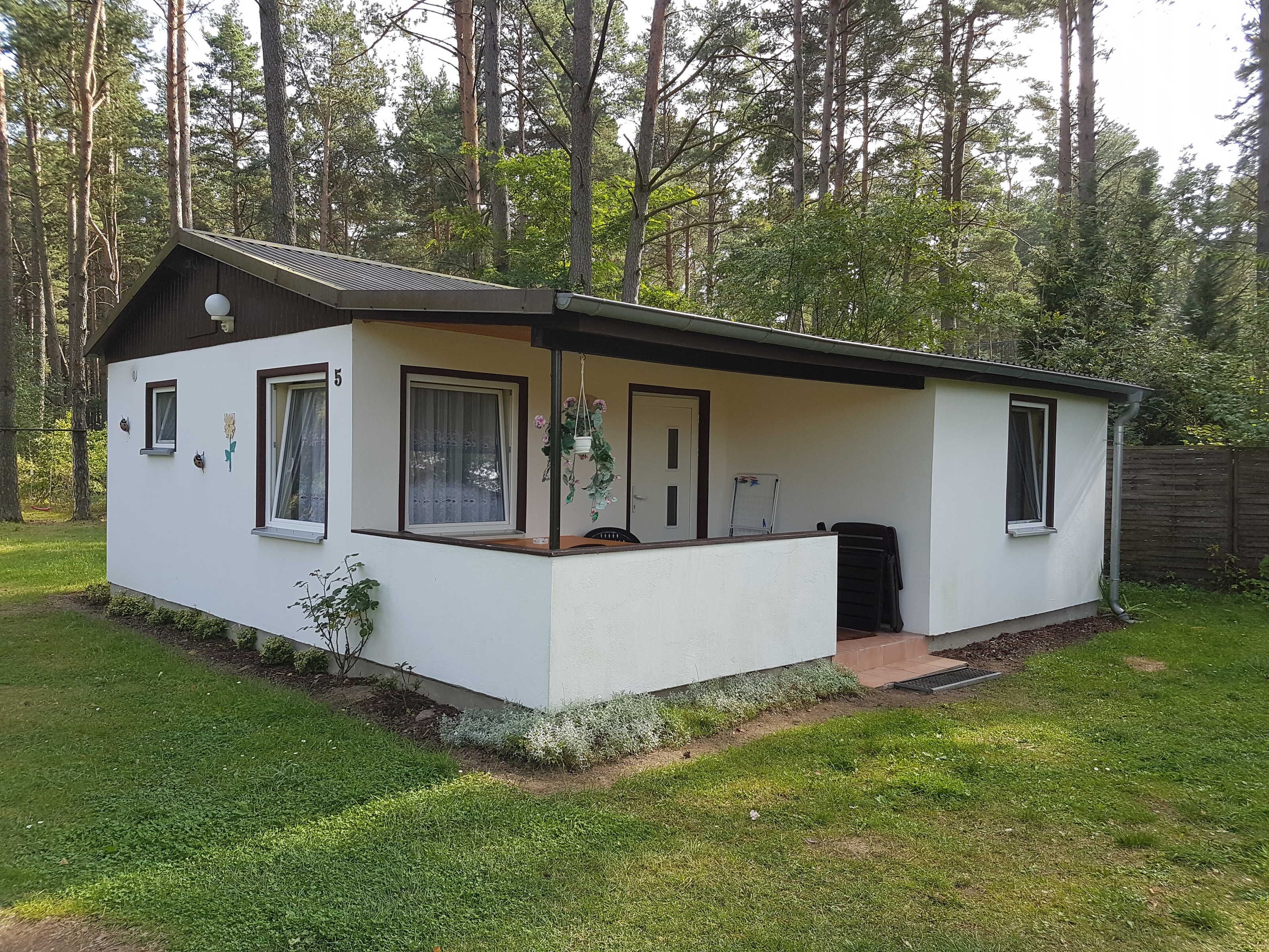 Une petite maison de plain-pied, avec un toit en pente, un porche et un petit jardin devant.