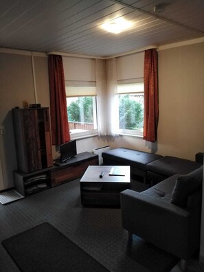 Una sala de estar con un sofá, una mesa de centro, un televisor y una ventana con cortinas.