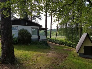 A house with a white exterior, a covered porch, and a small shed in a wooded area.