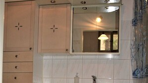 Un baño con armarios color beige, un lavamanos blanco, un espejo y una alfombra negra.