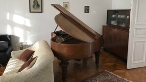 Un piano de cola en una sala de estar con un sofá, un aparador con puertas de vidrio y cuadros enmarcados en la pared.