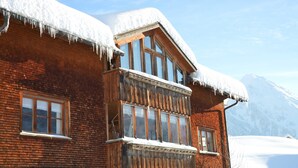 Eine Holzhütte mit Balkon, großen Fenstern und einem verschneiten Berg im Hintergrund.