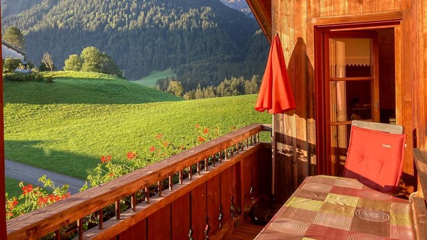 Eine Holzhütte mit einem Balkon mit Blick auf ein grünes Tal und Berge.