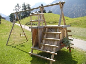 Une structure de jeu en bois, installée dans un espace verdoyant, avec une montagne en arrière-plan.